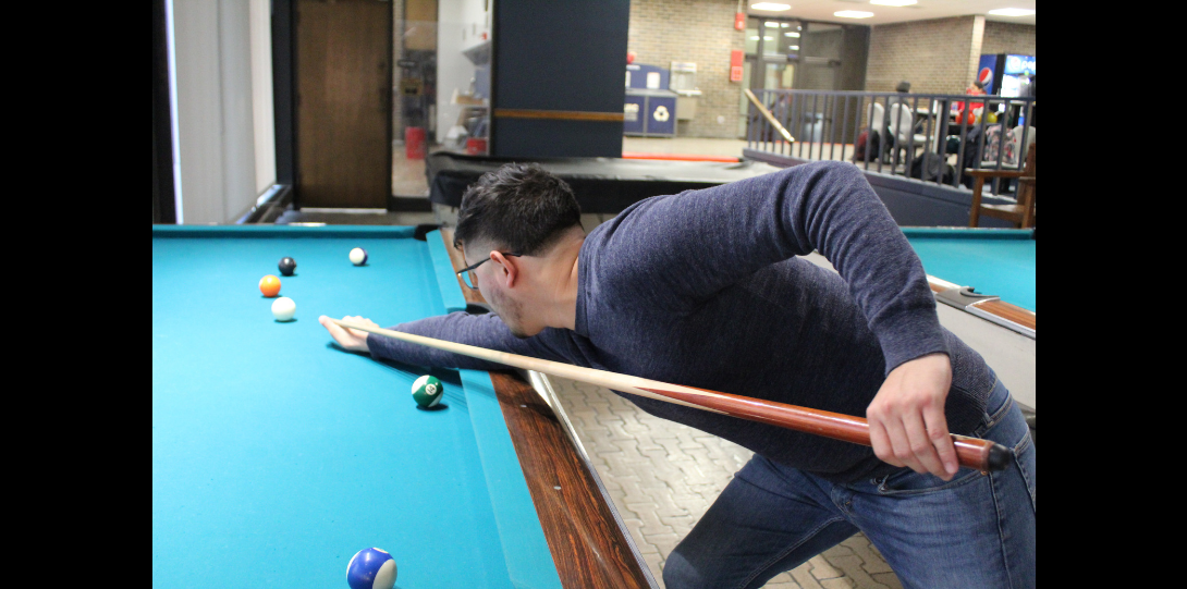 Hispanic male focusing on making a pool shot.
